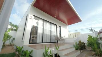 Una casa moderna con techo rojo, grandes puertas correderas de vidrio y una terraza de madera.