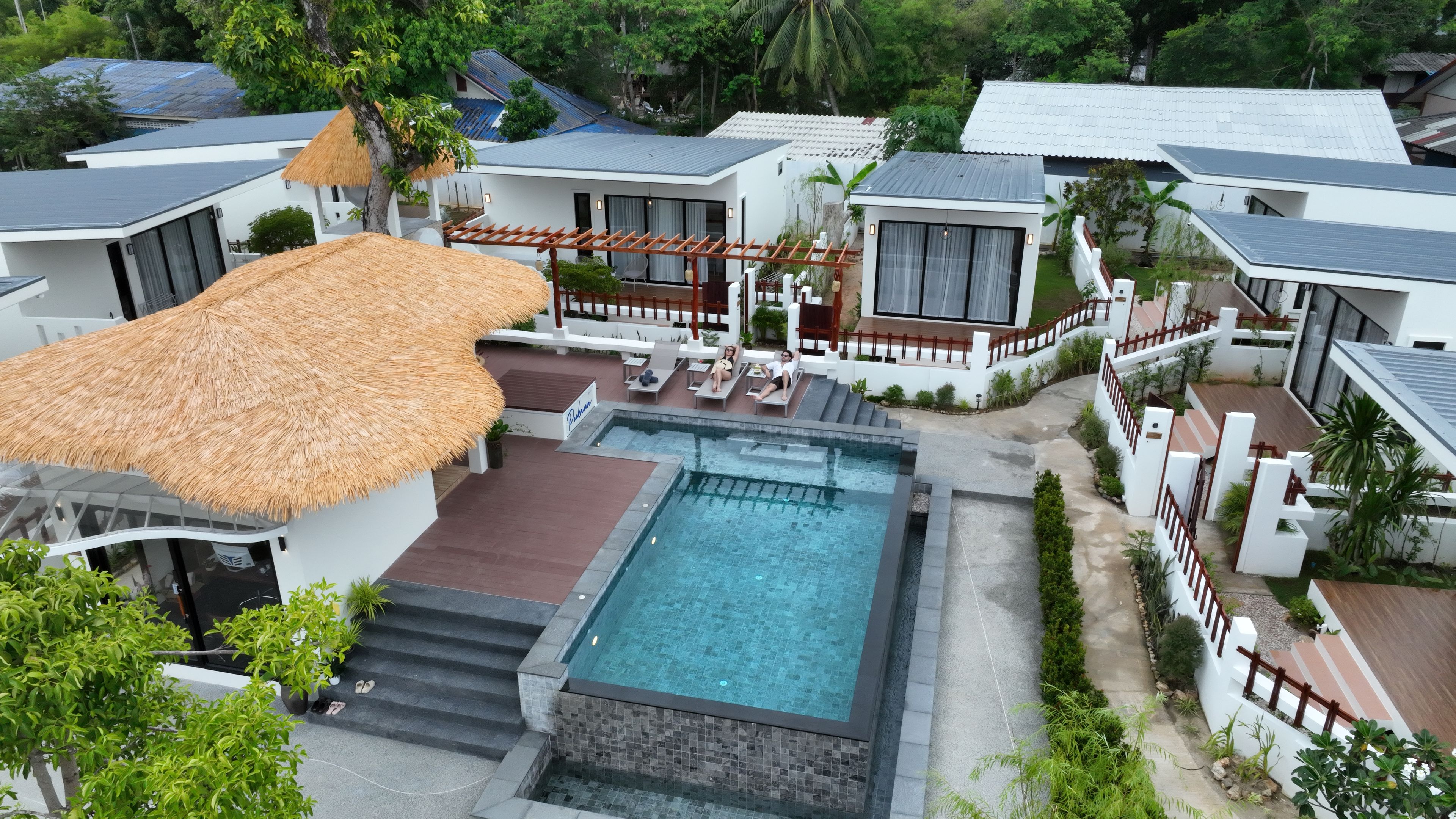 Un resort moderno con piscina, estructuras de techo de paja y un jardín bien cuidado.