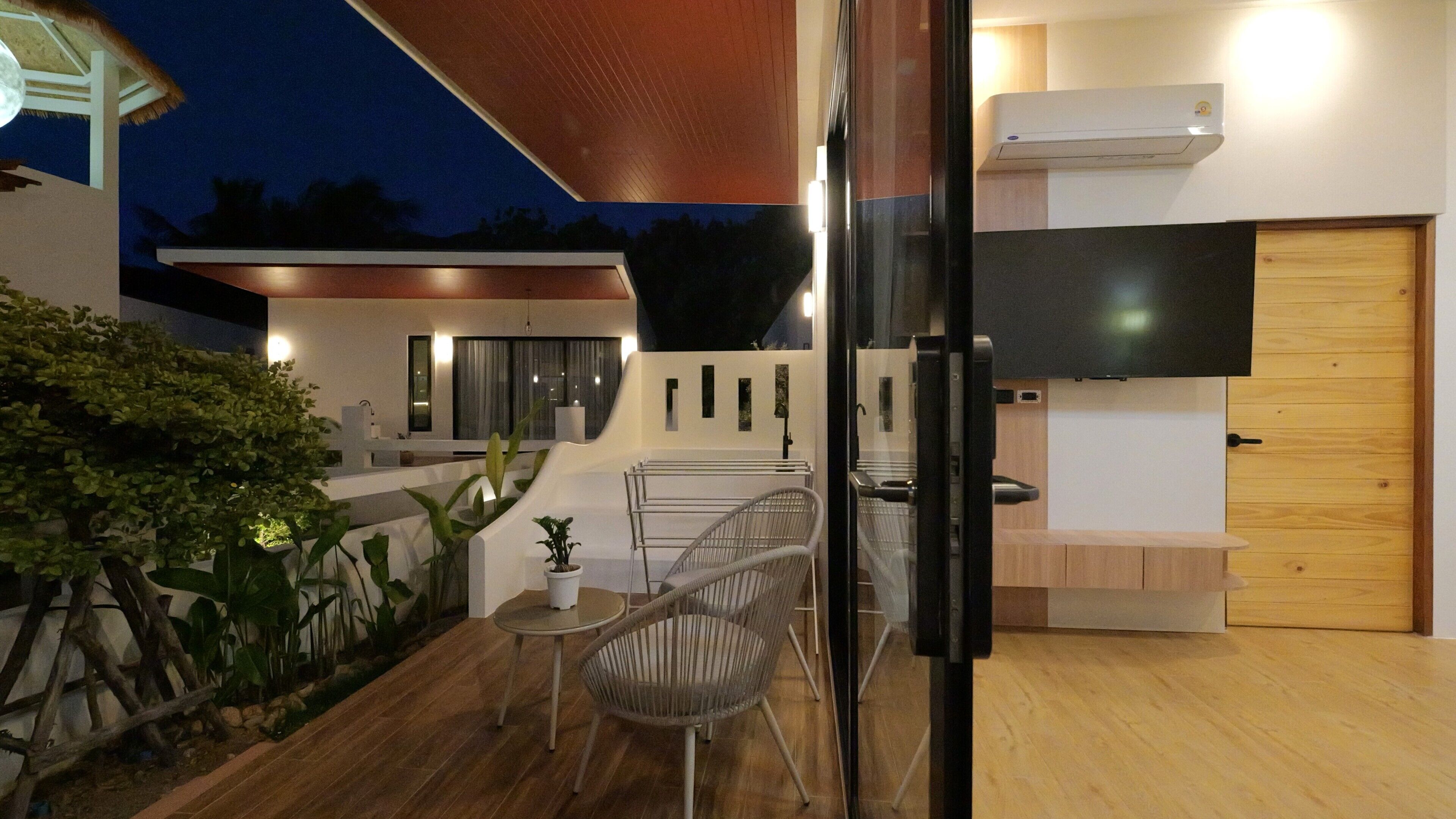 Un patio exterior con zona de comedor, televisor en la pared y puerta de madera.