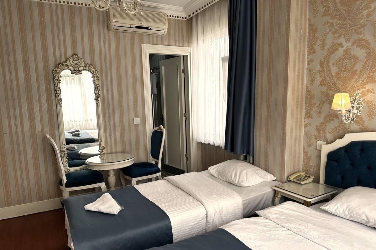 Camera d'albergo con due letti, un'area salotto con tavolo e sedie, uno specchio e un telefono.