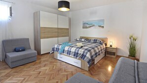 A bedroom with a bed, a sofa, a wardrobe, a nightstand, and a potted plant. - Apartment with garden and BBQ area (Umag)