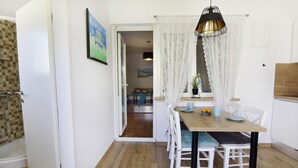 A dining area with a wooden table, white chairs, a pendant light, and a view into the adjacent room. - Apartment with garden and BBQ area (Umag)
