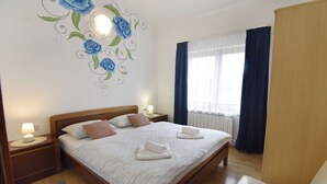 Camera d'albergo con un letto grande, due comodini con lampade, una testiera in legno, una finestra con tende e un muro decorato con un murale floreale.