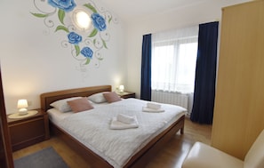 Een hotelkamer met een groot bed, twee nachtkastjes met lampen, een houten hoofdbord, een raam met gordijnen en een wand met een bloemig muurschildering.