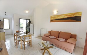 Een woonkamer met een bank, een glazen salontafel en een eethoek met een tafel en stoelen.