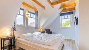 Ein Schlafzimmer mit einem Bett, einem Nachttisch, einer Lampe und zwei Fenstern.