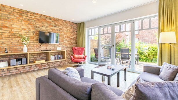 Ein modernes Wohnzimmer mit Backsteinwand, Flachbildfernseher, rotem Sessel und Sofa.