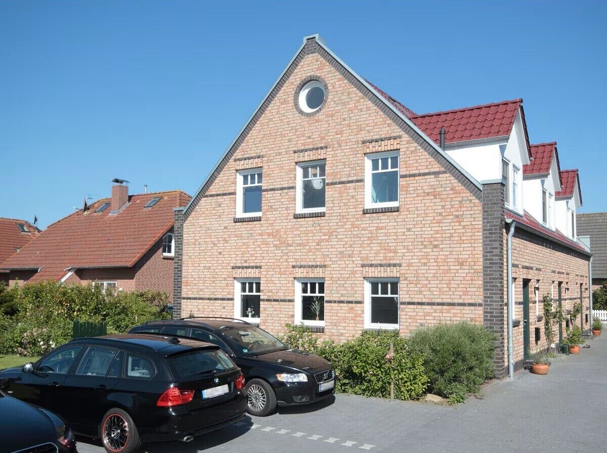 A brick building with a pitched roof, multiple windows, and a parking area with cars.