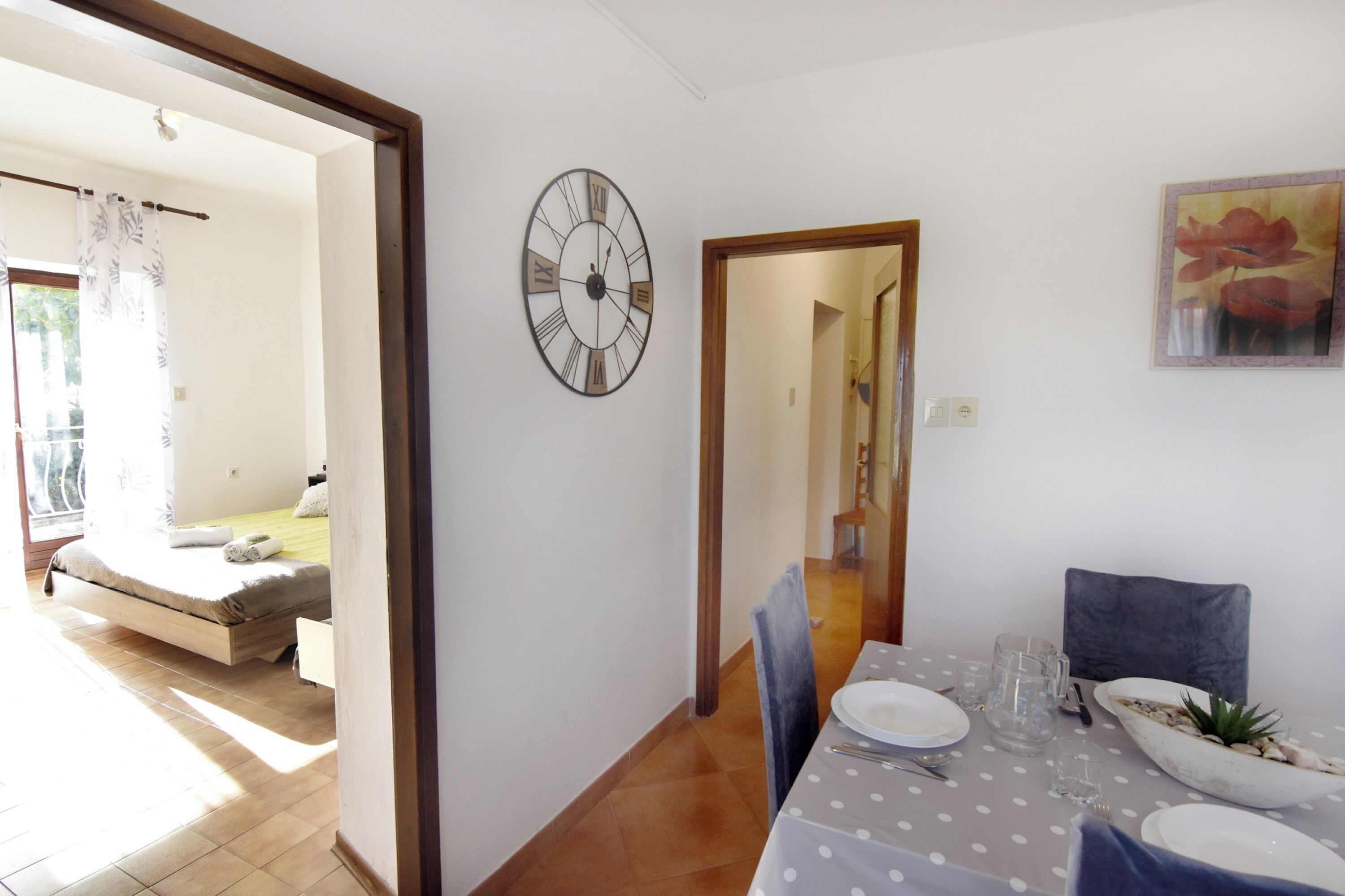 Ein Zimmer mit einem Bett, einem Esstisch für zwei Personen, einer Wanduhr und einem Gemälde.