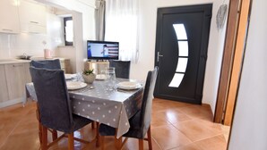 A dining area with a table set for four, a television, and a kitchen in the background. - Green retreat near the coast (Bašanija)