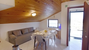 Habitació amb sostre de fusta, un sofà, taula de dinar amb cadires, televisió i una porta que dóna a l'exterior.