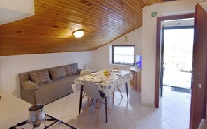 Une pièce avec un plafond en bois, un canapé, une table à manger avec des chaises, un téléviseur et une porte donnant sur l’extérieur.