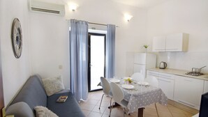 A compact living space with a sofa, dining table, chairs, a kitchenette, and a door leading to an outdoor area. - Ground-floor retreat surrounded by nature (Bašanija)