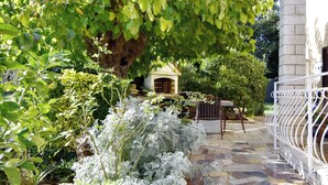 A stone patio with a white metal fence, a wooden bench, and a small garden area with various plants. - Ground-floor retreat surrounded by nature (Bašanija)