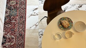 Un tavolo rotondo con un piatto decorato con motivi floreali, un bicchiere, una tazza, un tappeto fantasia e una sedia con schienale in legno.