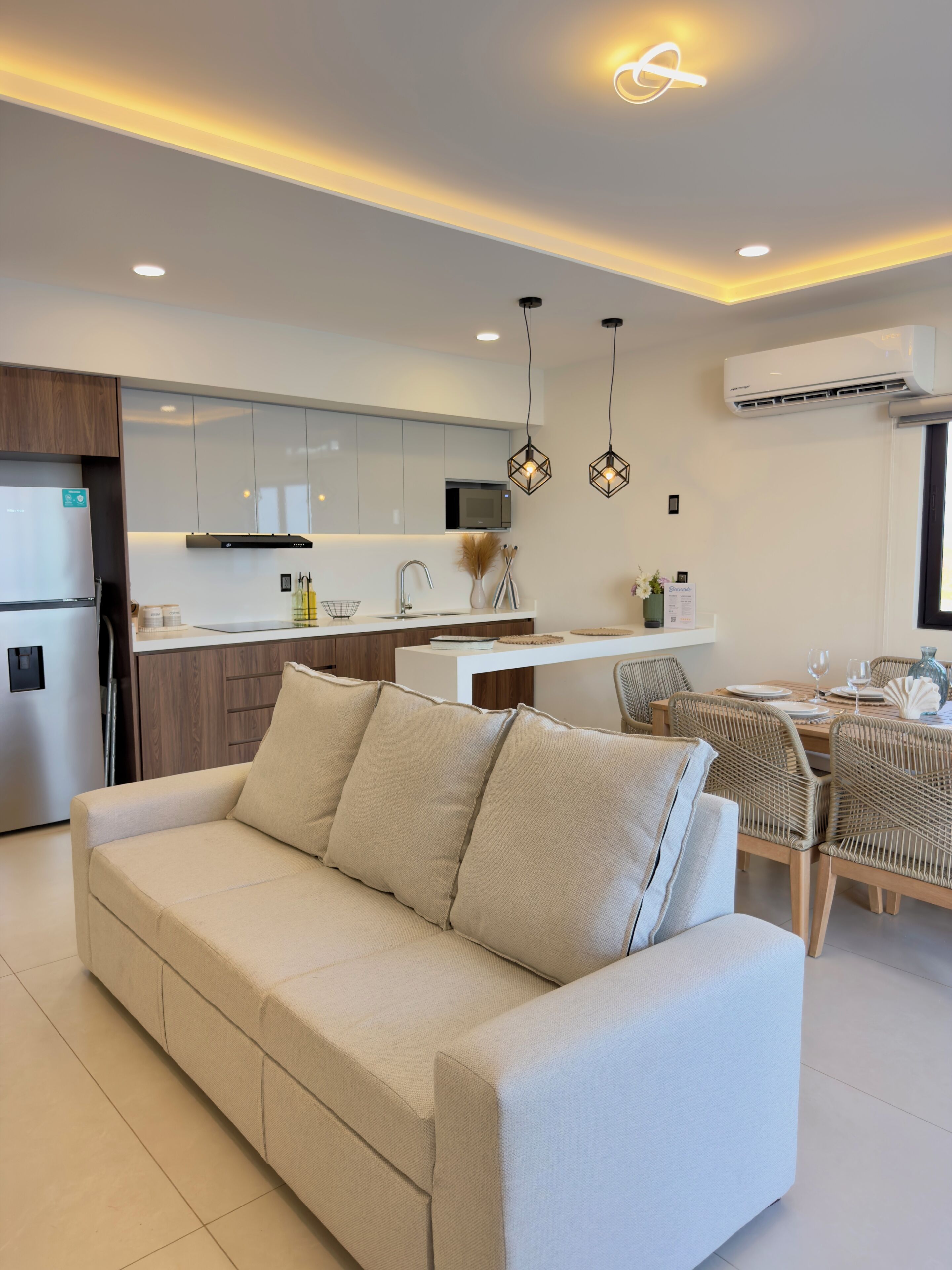 Uma cozinha moderna com micro-ondas embutido, área de refeições com mesa e cadeiras, e um sofá bege.
