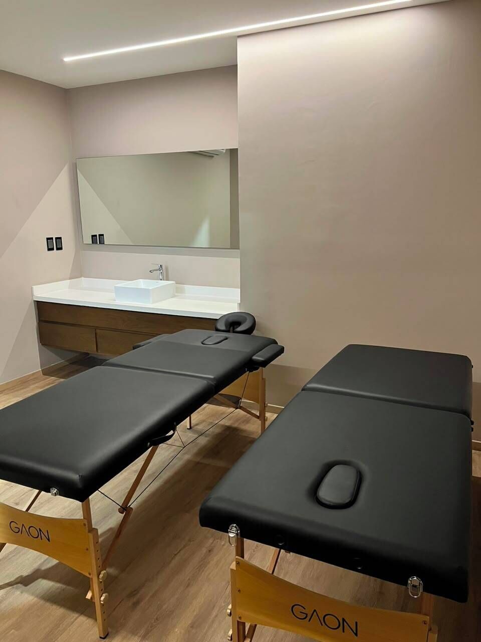 A clinical examination room with two examination tables, a white sink, and a large mirror.
