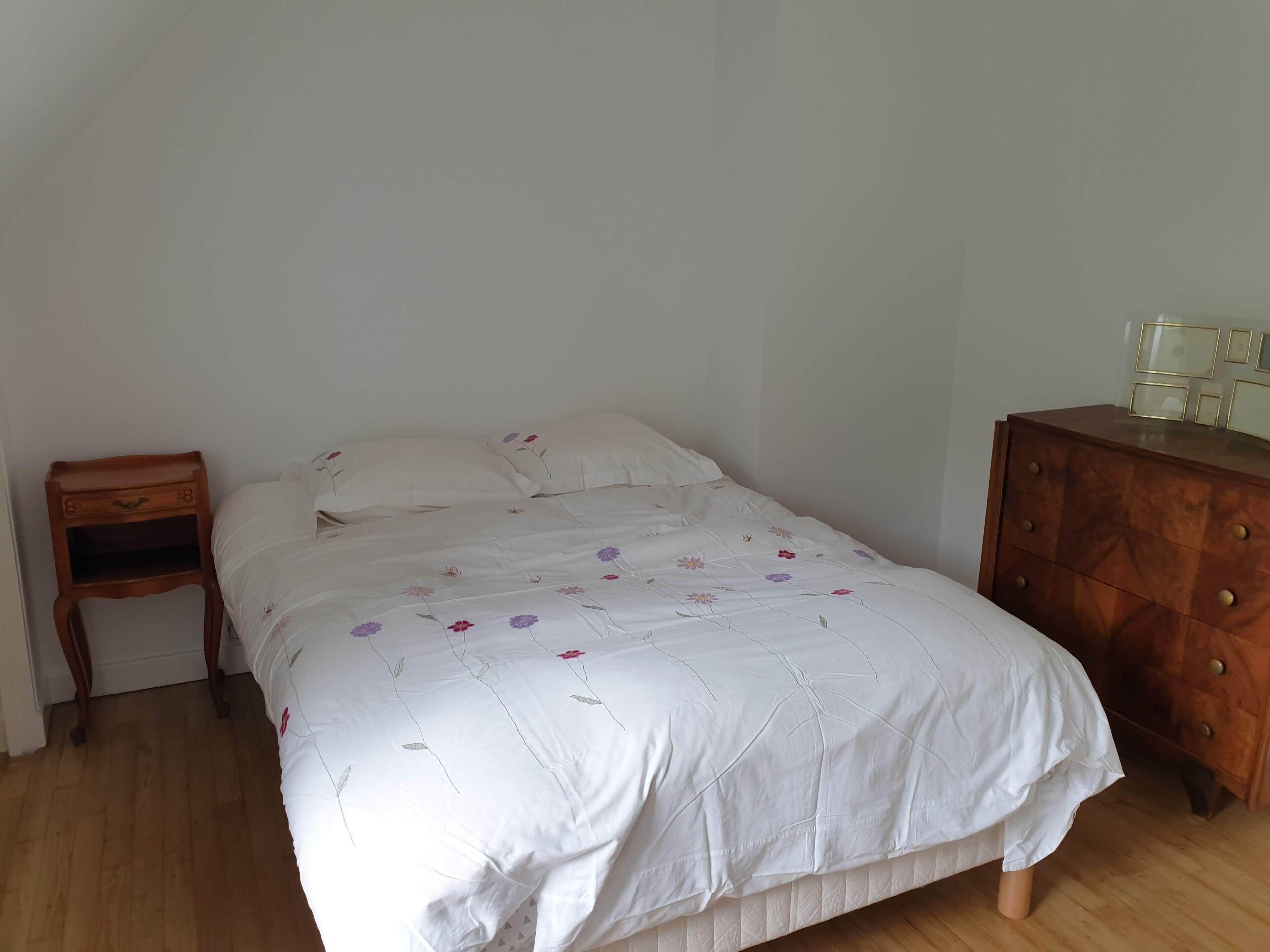 Ein Einzelbett mit Blumenmuster, ein Nachttisch aus Holz und eine Kommode mit Schubladen.