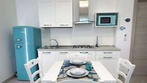 A compact kitchen with a blue refrigerator, white cabinets, a microwave, and a dining table set for two. - Casa Pantano - Agriturismo (Marina di Casal Velino)