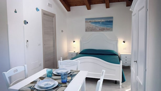 A bedroom with a bed, bedside tables, a painting, and a dining area with chairs and plates. - Casa Pantano - Agriturismo (Marina di Casal Velino)