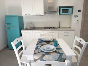 A compact kitchen with white cabinets, a teal refrigerator, a microwave, and a dining table set with plates and glasses.