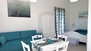 A room with a teal sofa, a white dining table with chairs, a white bed, and a painting on the wall. - Casa Pantano - Agriturismo (Marina di Casal Velino)