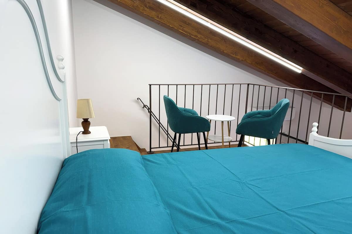 Un dormitorio con una cama, dos sillas, una mesita y una mesita de noche.