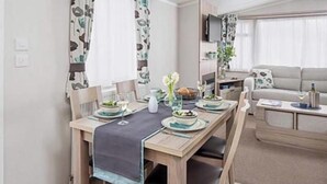 Un coin repas avec une table dressée pour deux personnes, un canapé et un téléviseur en arrière-plan.