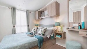 Ein Schlafzimmer mit einem Bett, Nachttischen, einem Spiegel und einem Fenster mit Vorhängen.