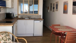 Une cuisine compacte avec des meubles blancs, un lave-vaisselle et un coin repas comprenant une table et des chaises rouges.