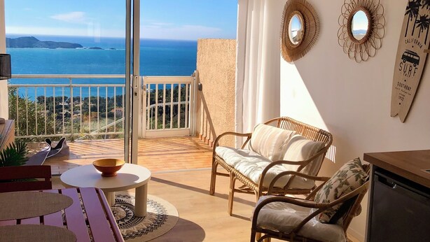 Un balcon avec vue sur l’océan, des meubles en osier, une table ronde et un luminaire suspendu au plafond.