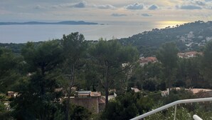 Un paysage côtier avec vue sur la mer, une zone vallonnée parsemée de bâtiments et de grands arbres aux feuillages denses.
