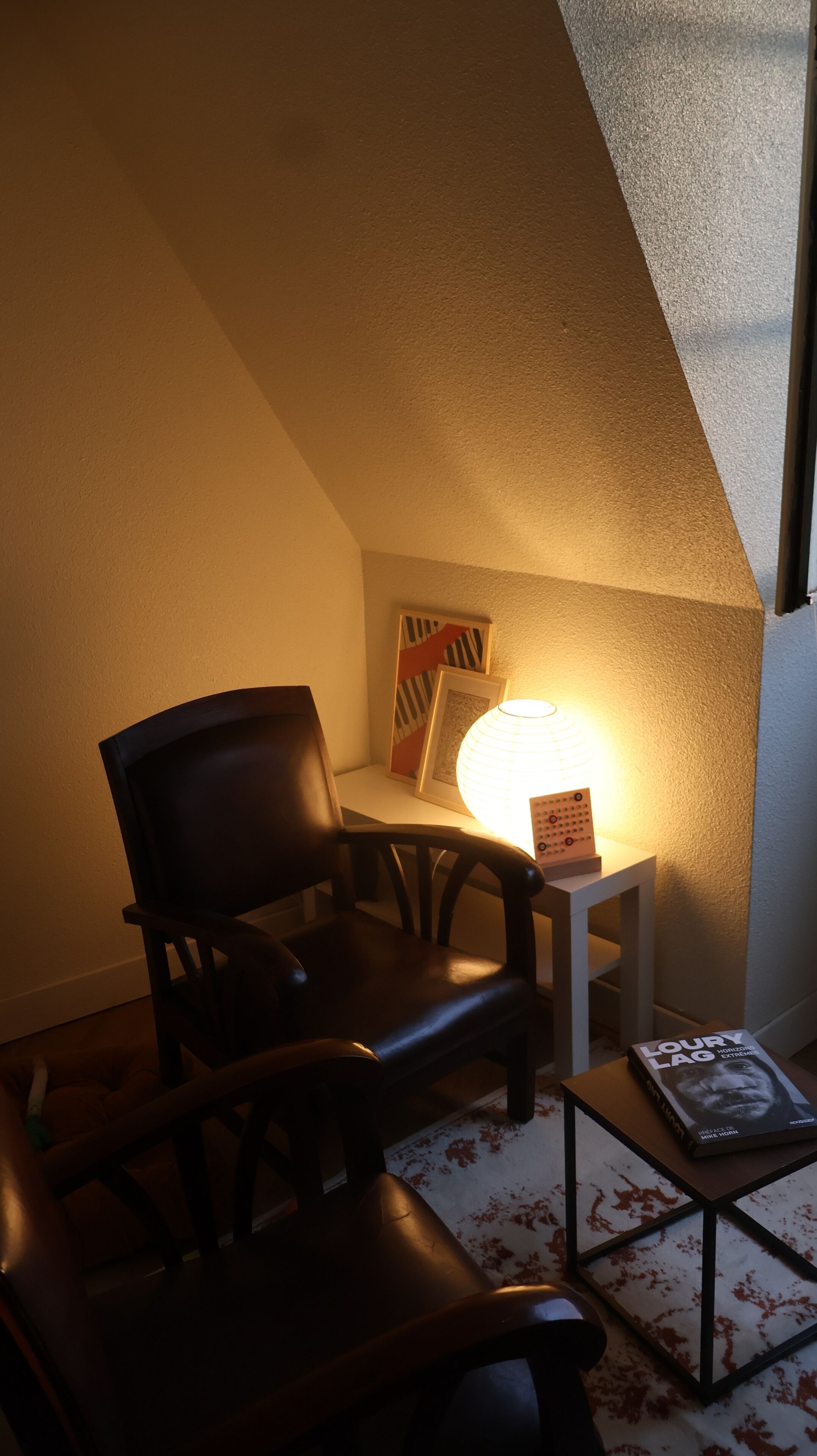 Ein Zimmer mit einem dunkelbraunen Ledersessel, einem kleinen Tisch mit einer Lampe, einem gerahmten Bild und einem Buch auf dem Tisch.