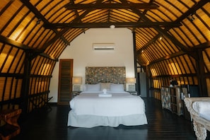 A spacious room with a high ceiling, a large bed, a decorative headboard, and a wooden floor.