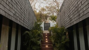 A narrow pathway flanked by wooden walls leading to a gate, with steps illuminated by lights and surrounded by greenery.