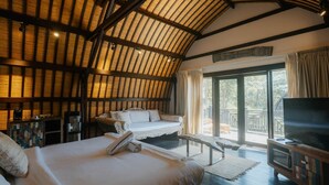 A bedroom with a large bed, a TV, a wooden ceiling, and a view of the outdoors.