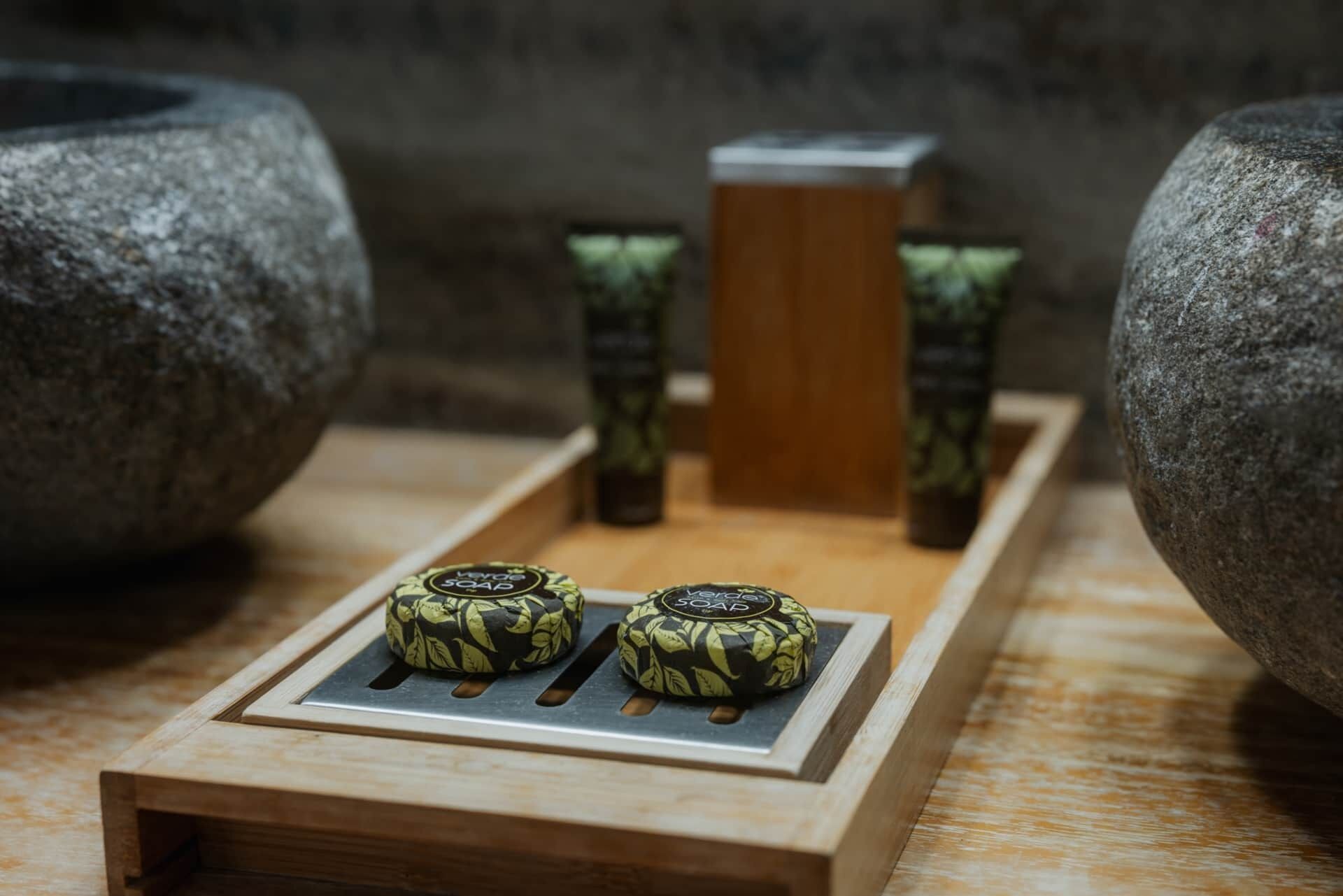 A wooden tray with two soap bars and a wooden block, surrounded by stone bowls.