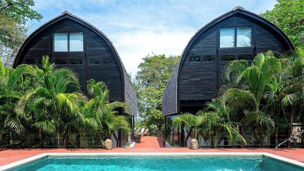 A symmetrical building with a pool in front, surrounded by tropical vegetation.
