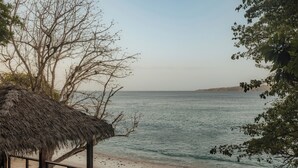 A beach view with a thatched-roof structure, sandy beach, and calm sea.