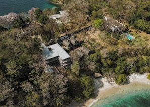 An aerial view of a coastal property with multiple buildings, a swimming pool, and a beach.