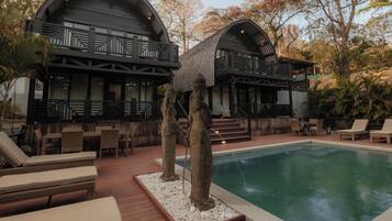 Zona de piscina con sillones de descanso, una alberca y un edificio con balcón.