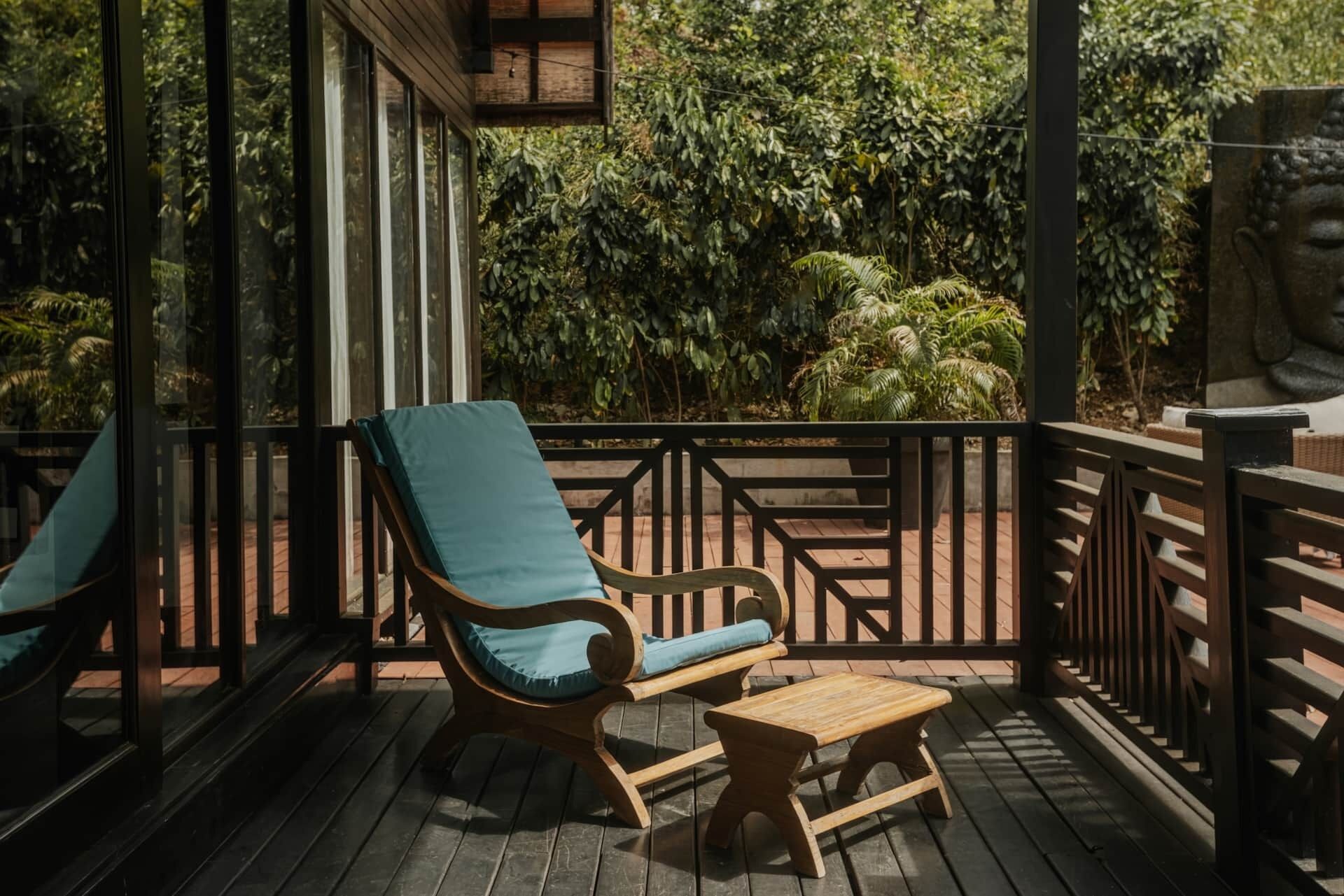 Una terraza de madera con dos sillones de descanso y una pequeña mesa, rodeada por una barandilla y con vistas a un exuberante jardín.