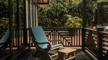 Una terraza de madera con dos sillones de descanso y una pequeña mesa, rodeada por una barandilla y con vistas a un exuberante jardín.