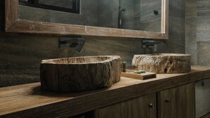 Ein Badezimmer mit einem Holzkosmetikschrank, einem großen Spiegel und einem Becken aus Stein.