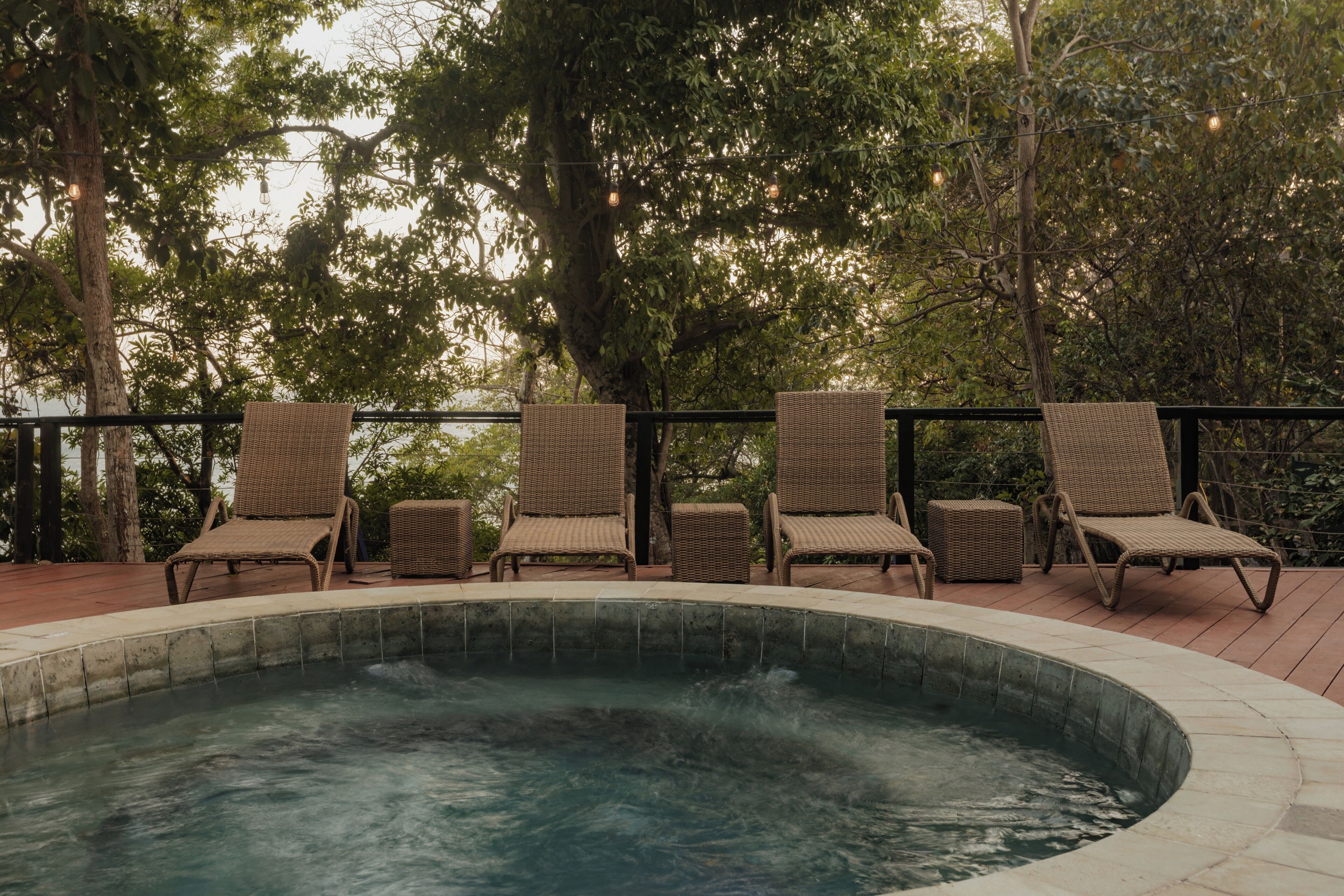 A hot tub surrounded by wicker chairs on a wooden deck, with trees in the background.