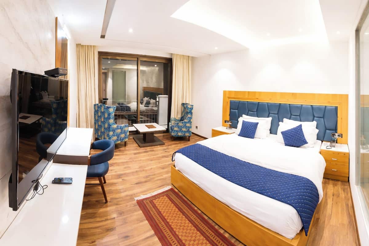 A hotel room with a bed, a TV, a desk, and a seating area with chairs.
