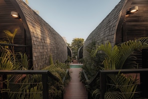 A pathway leading to a pool surrounded by wooden structures and tropical plants.