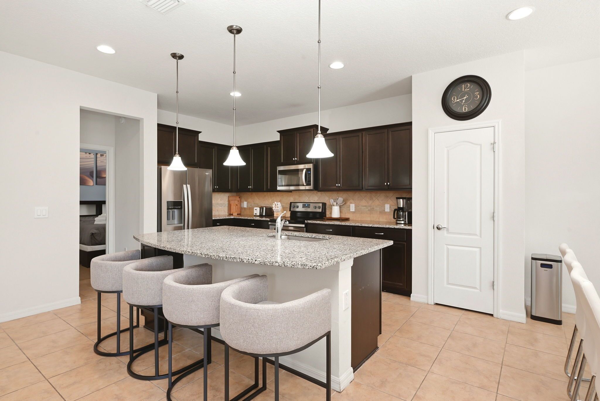 A modern kitchen with a central island, bar stools, dark cabinets, stainless steel appliances, and pendant lighting.