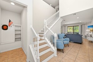 A staircase with white railings, a blue sofa, and a window with a view of greenery. - Windsor at Westside Resort 5 Bed Home w/ 3 King Suites & Private Pool Near Disney (Kissimmee)