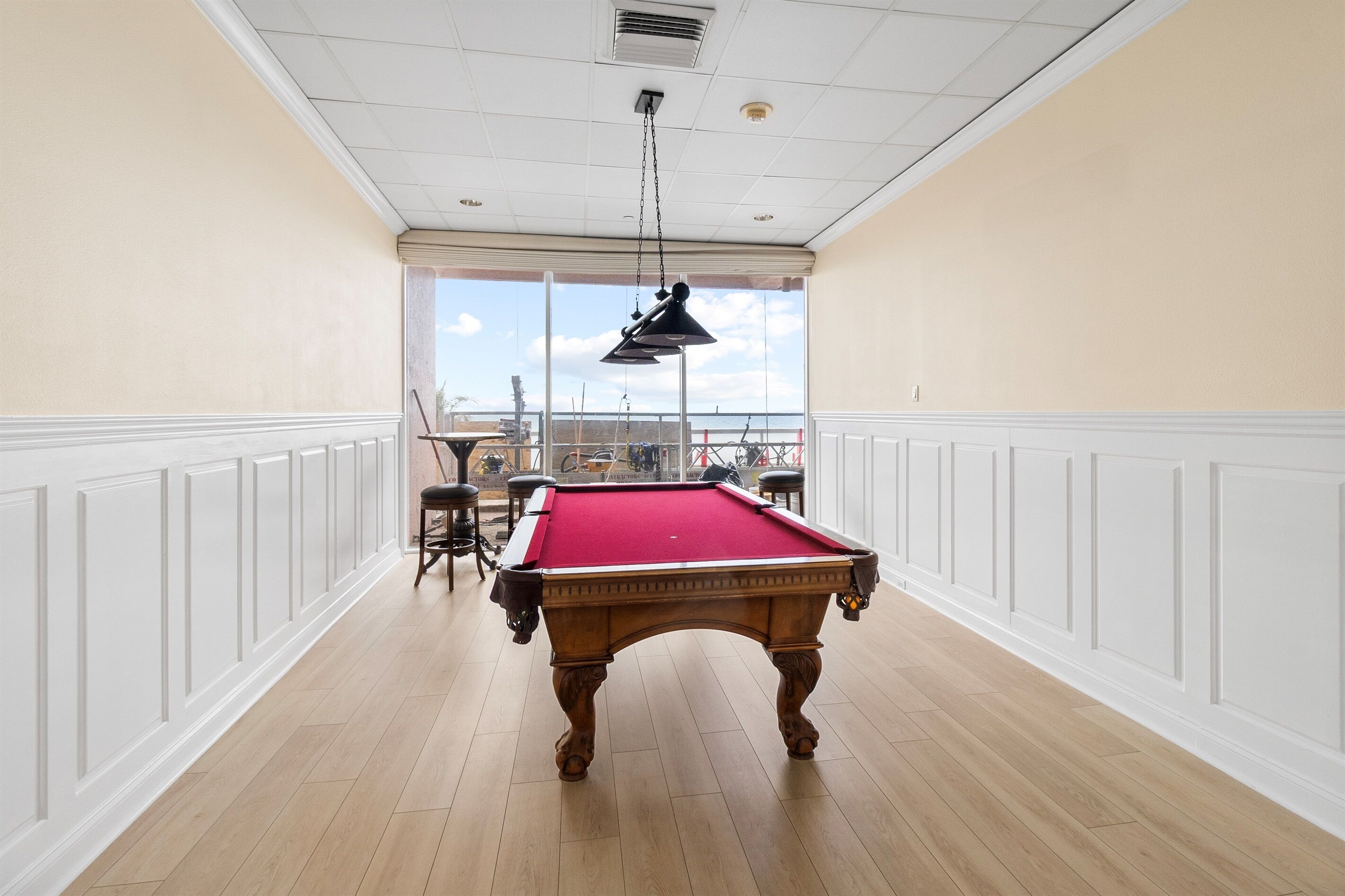 Una mesa de billar en una habitación con paneles blancos y vistas amplias por las ventanas.
